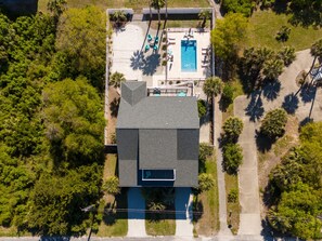 Vista aérea de uma casa com piscina, cercada por árvores e um gramado bem cuidado.