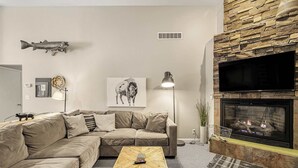 A living room with a sectional sofa, a herringbone coffee table, a fireplace, a mounted television, and a wall-mounted fish decoration. - Park Place - 20 Miles to YNP ~ Hot Tub ~ Wi-Fi ~ Fire Pit (Island Park)