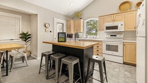 A kitchen with wooden cabinets, a microwave, an oven, and a dining area with stools. - Park Place - 20 Miles to YNP ~ Hot Tub ~ Wi-Fi ~ Fire Pit (Island Park)