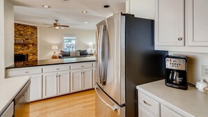 A modern kitchen with a stainless steel refrigerator, a coffee maker, and a brick wall backsplash. - BREATHTAKING VIEWS AT NORMANDY BREEZE! (Denver)
