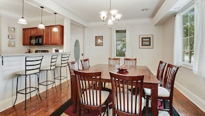 Un comedor con mesa y sillas de madera, una cocina con microondas y lámparas colgantes.