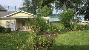 Ein kleines, gelbes Haus mit einer Veranda, umgeben von einem gepflegten Garten mit verschiedenen Pflanzen und Blumen.