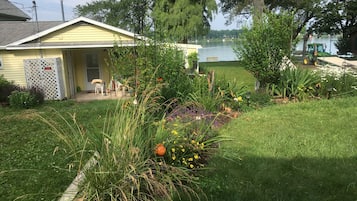 Enjoy a serene garden with a variety of plants and flowers, a lawn chair, and a scenic view of the water.