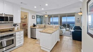 A modern kitchen with white cabinetry, a granite countertop, and a view of the ocean. - Beach Club 503 - 𝑩𝒍𝒖𝒆 𝑳𝒂𝒈𝒐𝒐𝒏 (Pensacola Beach)
