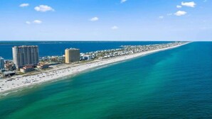 An aerial view of a coastal area with a long beach, several high-rise buildings, and a clear blue sky. - Beach Club 503 - 𝑩𝒍𝒖𝒆 𝑳𝒂𝒈𝒐𝒐𝒏 (Pensacola Beach)