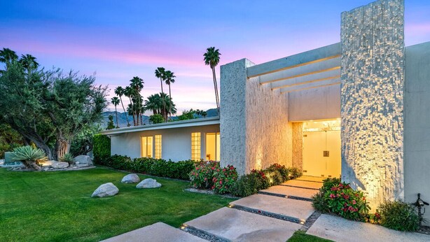 Une maison moderne avec une façade en pierre, une pelouse bien entretenue et un chemin menant à l’entrée.