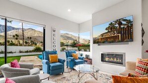 Un salon moderne avec une cheminée, des canapés bleus et gris, une table basse en verre et une grande fenêtre donnant sur une vue imprenable sur les montagnes.