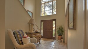 A hallway with a wicker chair, a lamp, a wooden door, and a large window.