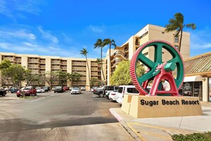 A parking lot with cars, a large gear sculpture, and a building labeled 'Sugar Beach Resort.' - Squeaky clean ground floor Sugar Beach #104 (Kihei)
