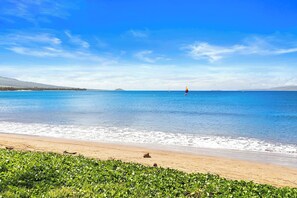 A beach with a clear sky, calm sea, and distant sailboat.