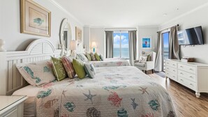 Ein Hotelzimmer mit zwei Betten, einem Fernseher, einem Schminktisch und Meerblick.