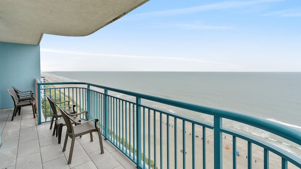 Een balkon met uitzicht op het strand, met een hekwerk en enkele stoelen.