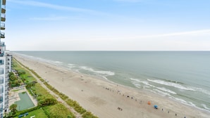 Een strand met een gebouw aan de linkerkant, een heldere lucht en de oceaan.