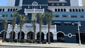 Een hotel met meerdere verdiepingen, een centraal torentje, een balkon en een bord met de tekst 'Paradise Resort'.