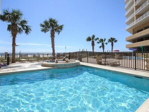 Relax by the pool with a view of the beach, surrounded by palm trees and a secure fence.
