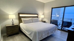 A bedroom with a bed, two bedside tables with lamps, a ceiling fan, and a large window with a view.