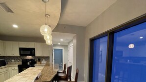 A modern kitchen with a large island, a dining area with chairs, and a view through large windows.