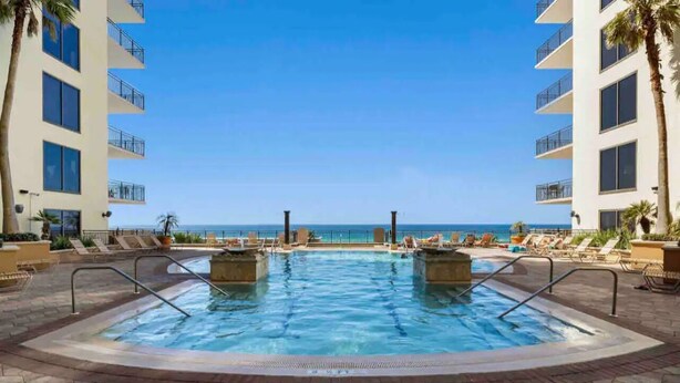 A pool area with two hot tubs, lounge chairs, and a view of the ocean.