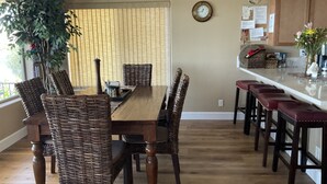 A dining area with a wooden table and wicker chairs, a kitchen with a white countertop, and a potted plant.