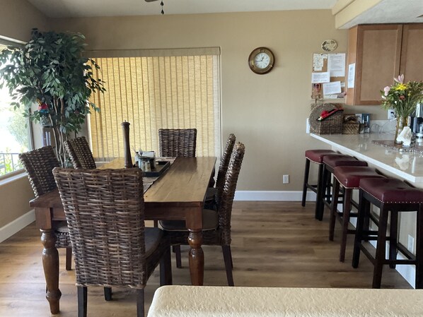 A dining area with a wooden table and wicker chairs, a kitchen with a white countertop, and a potted plant. - Bullhead City Riverfront Rental 4 Bedroom 3 Baths W/ Sandy Beach & private dock (Bullhead City)