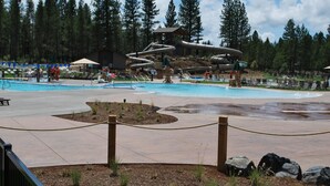 Un parque acuático con una piscina grande, toboganes y una cabaña de madera al fondo.