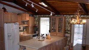 Una cocina con armarios de madera, un refrigerador, una mesa de comedor con sillas y una araña.