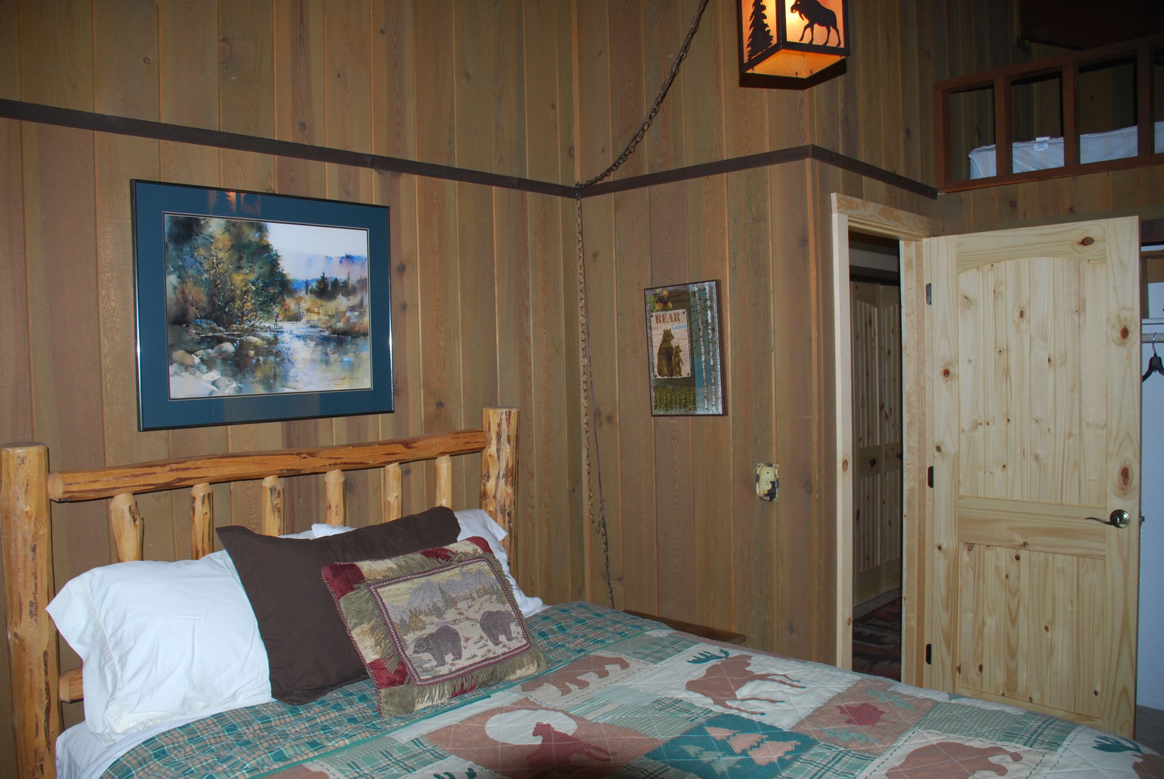 A wooden room with a bed, a framed picture of a landscape, and a door.