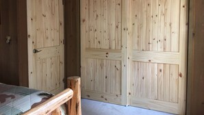 Una habitación de madera con dos puertas grandes, una cama con colcha estampada y un banco de madera.