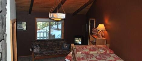 A cozy room with a wooden ceiling, a sofa, a bed with a floral bedspread, a TV, and a lamp.