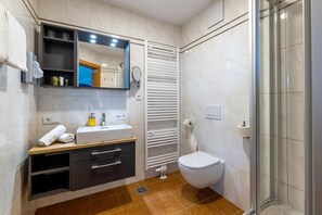 Une salle de bain moderne avec un lavabo blanc, un miroir et des toilettes, un porte-serviettes et un espace douche.