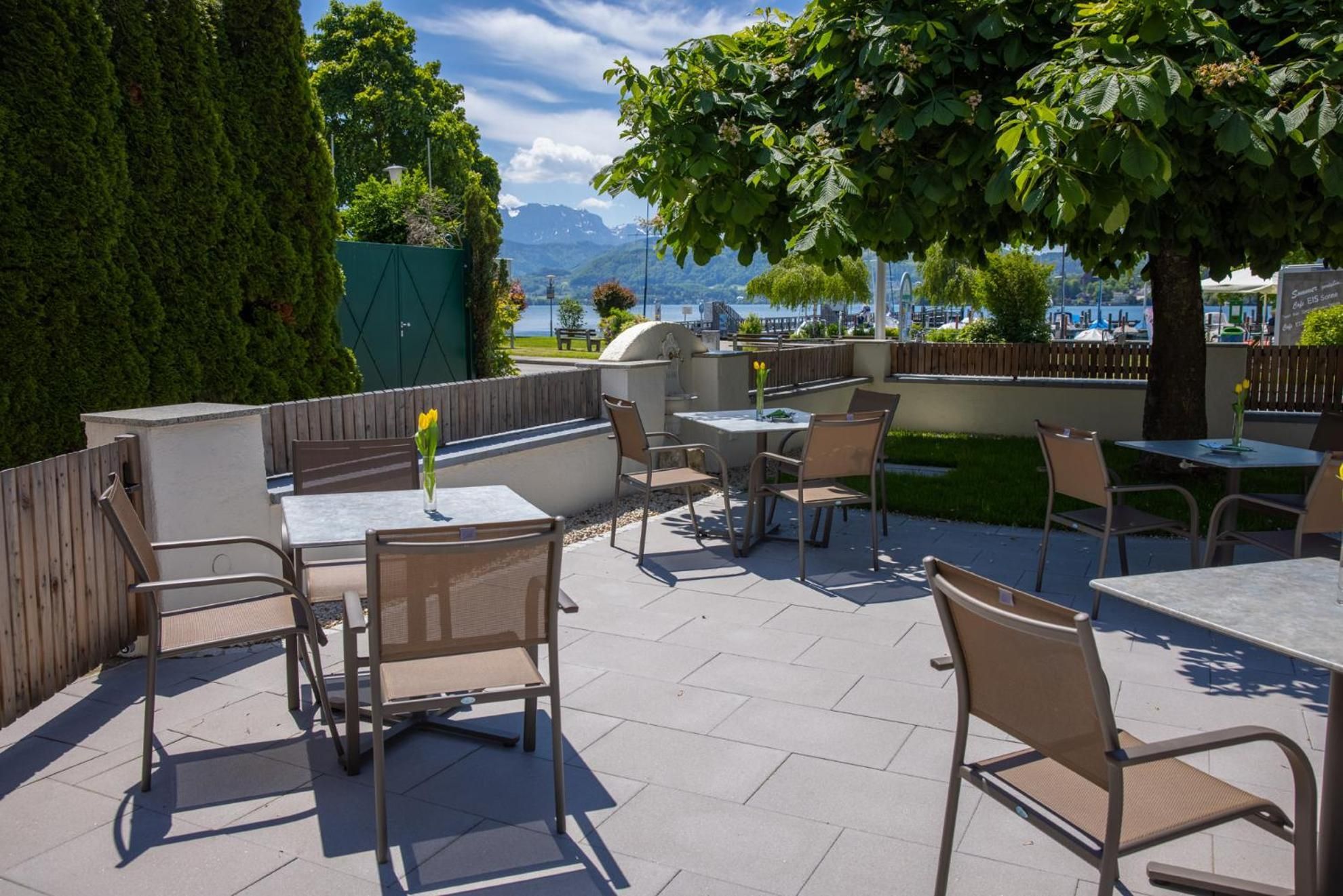 An outdoor patio with tables and chairs, a view of a lake, and a mountain in the background.