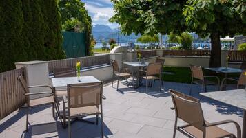 An outdoor patio with tables and chairs, a view of a lake, and a mountain in the background.