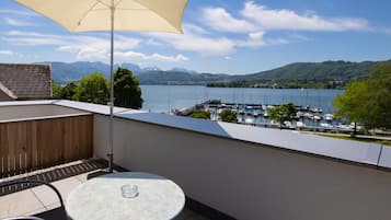 Ein Balkon mit Tisch und Stuhl, einem großen Sonnenschirm und Blick auf einen Jachthafen und Berge.