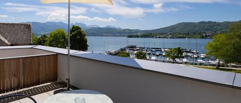 A balcony with a table and chair, a large umbrella, and a view of a marina and mountains.
