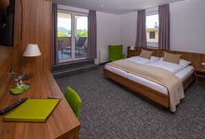 A hotel room with a bed, a desk with a lamp, a chair, a TV, and a view of the outdoors.