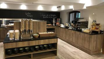 Ein Bereich mit Frühstücksbuffet, mit einer Holztresen, verschiedenen Speisen und einem Schild mit deutschem Text.