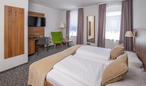 A hotel room with a bed, a desk, a chair, a television, and a mirror.