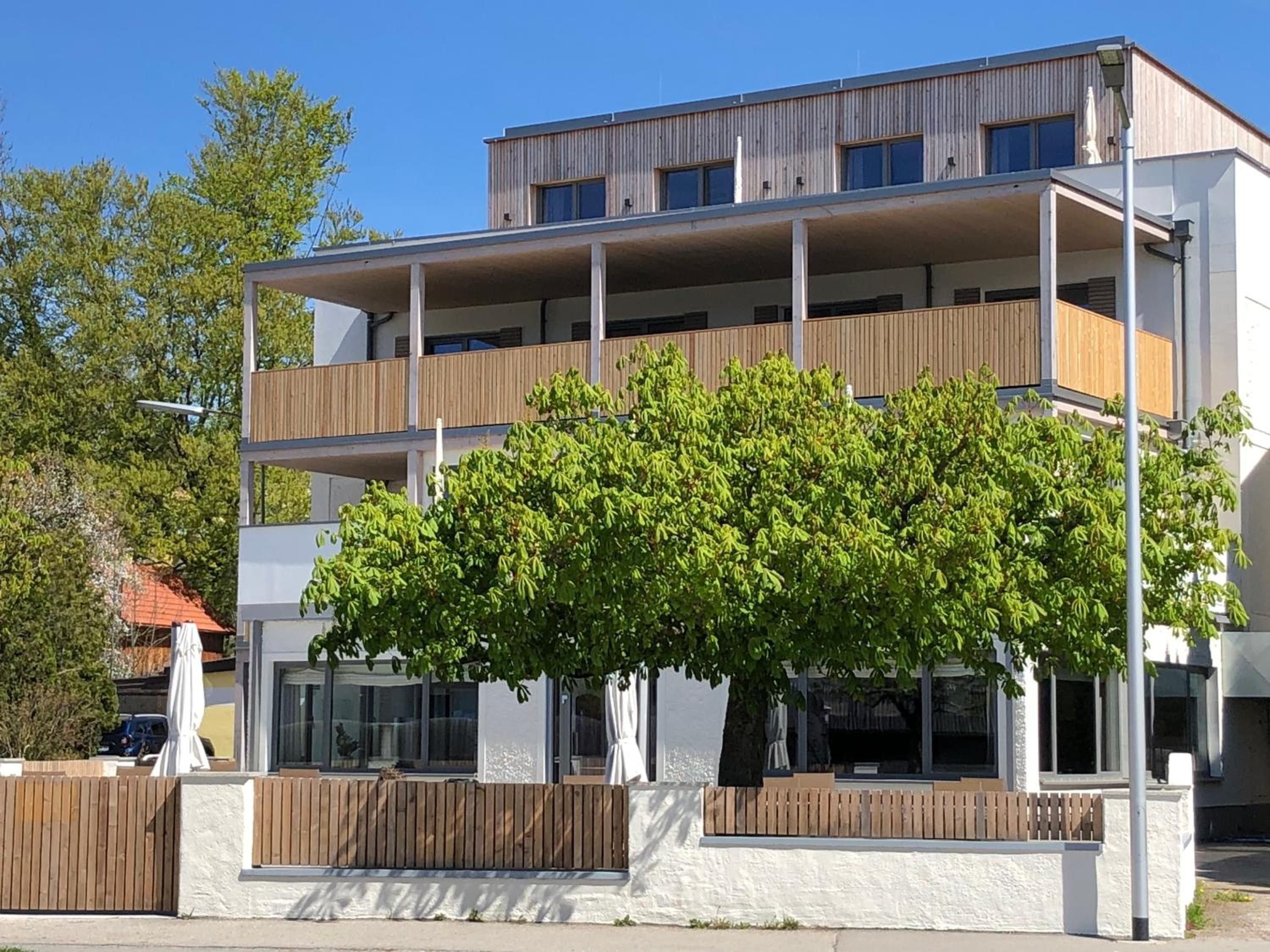 Ein mehrstöckiges Wohngebäude mit Balkonen, großen Fenstern und einem Baum im Vordergrund.
