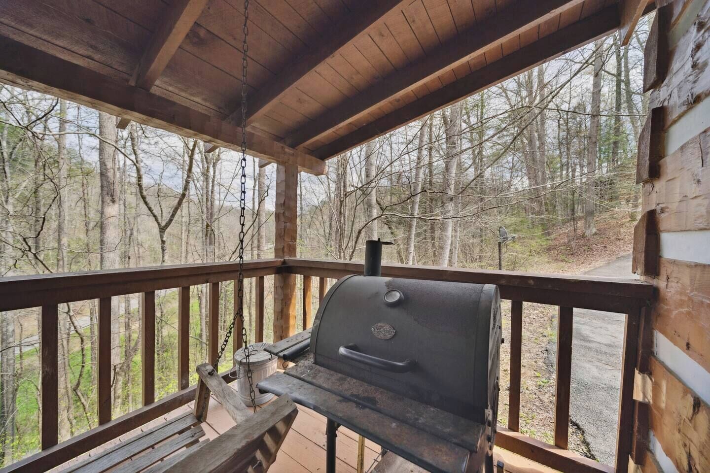 A wooden deck with a barbecue grill and a bench, overlooking a forested area.