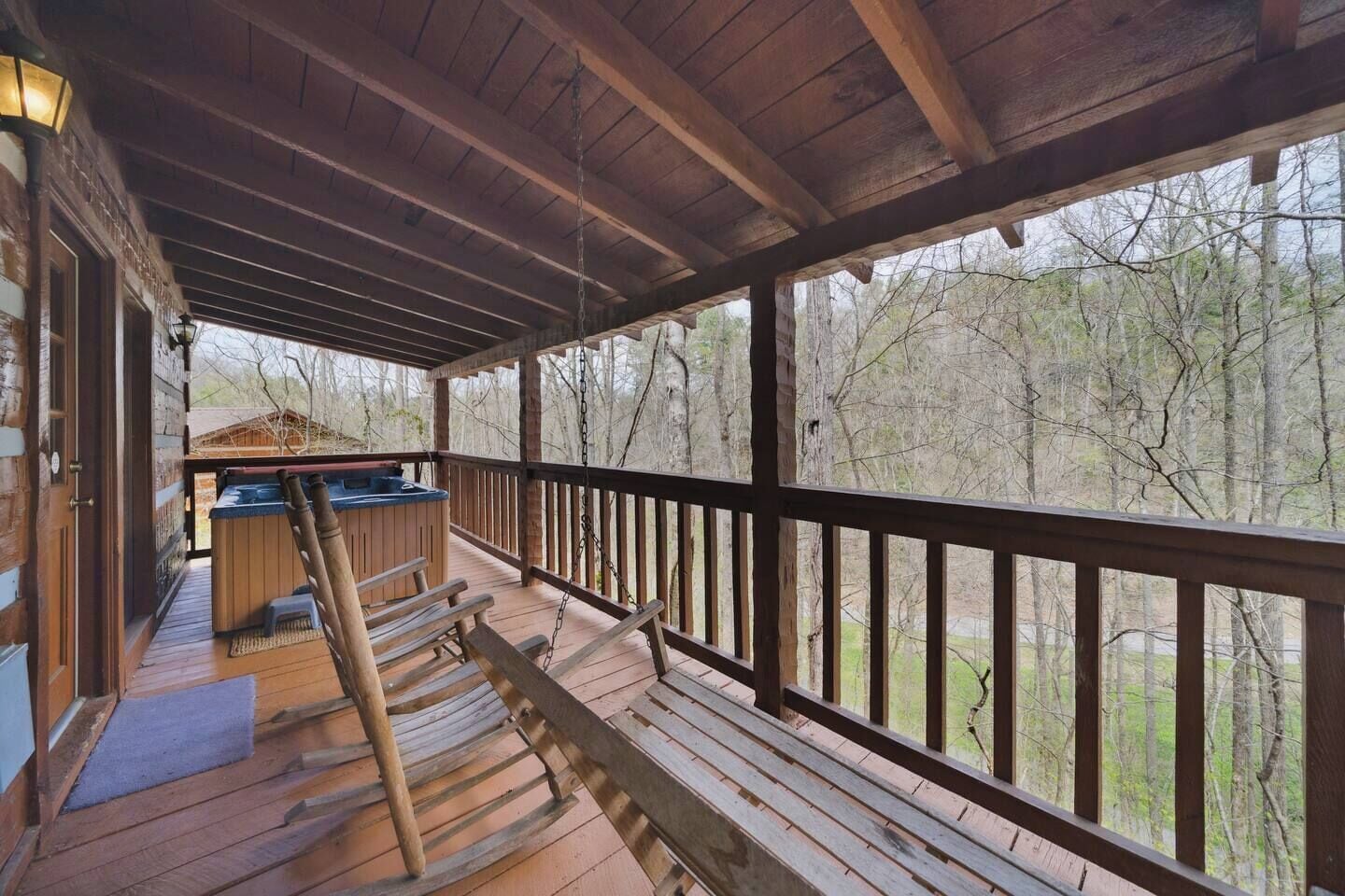 A wooden deck with a hot tub and seating area, overlooking a forested landscape.