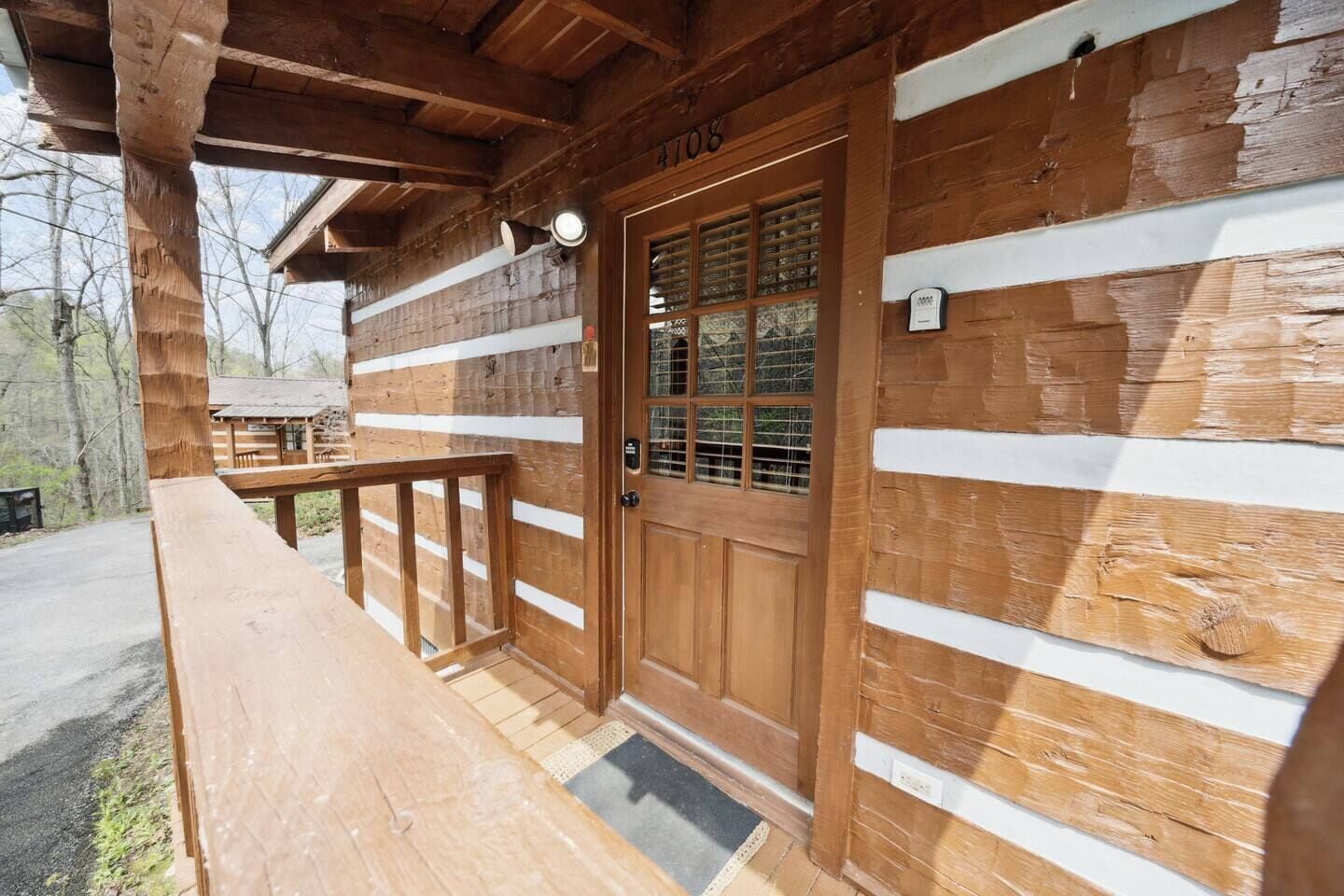Une cabane en bois avec une porte d’entrée portant le numéro « 108 », une terrasse en bois et une fenêtre à carreaux.