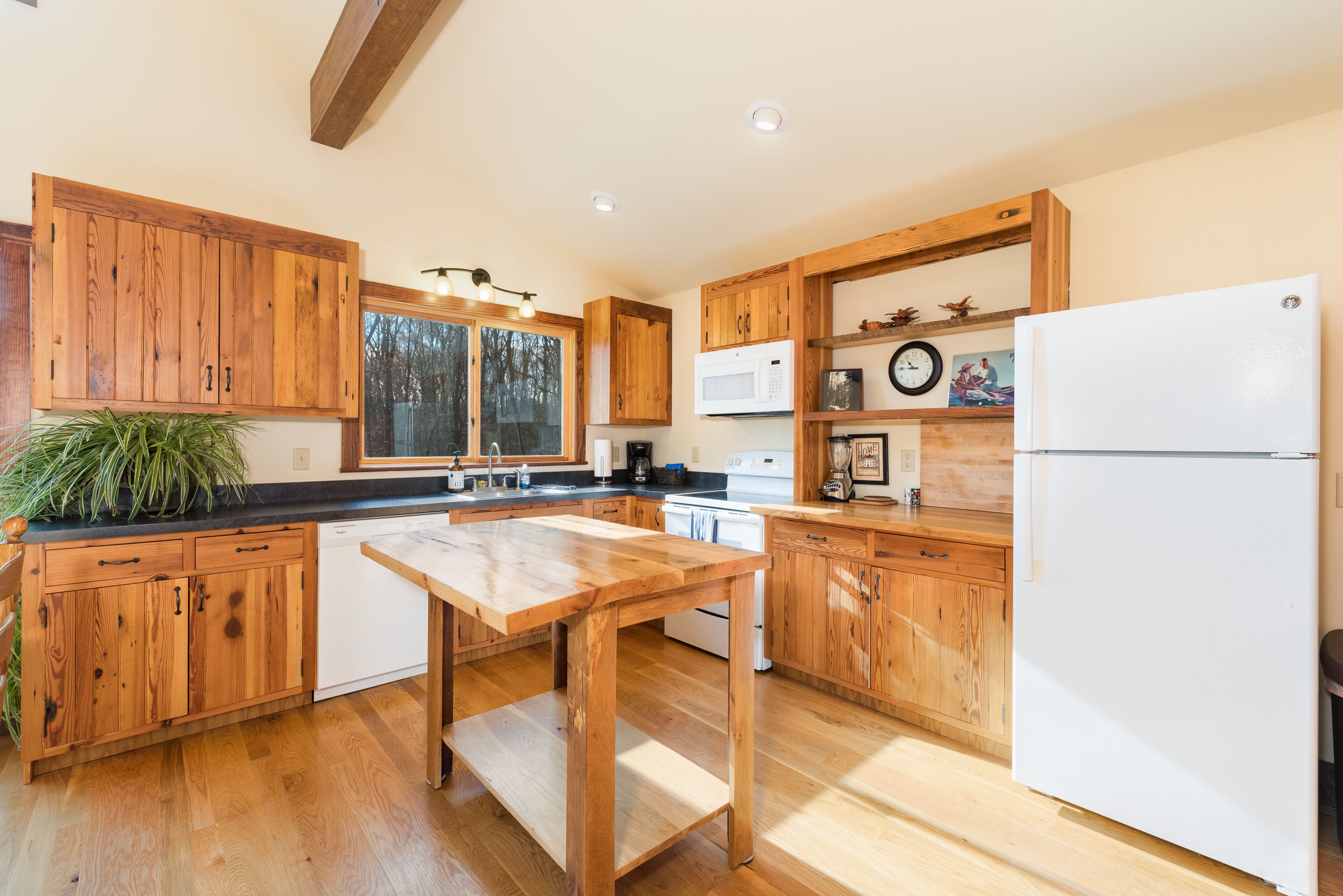 Une cuisine avec des meubles de rangement en bois, une table en bois, un réfrigérateur blanc et un four à micro-ondes.