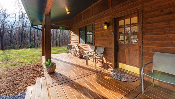 Une cabane en bois dotée d’une véranda, d’un espace salon extérieur et offrant une vue sur la forêt environnante.