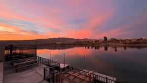 A waterfront view with a calm lake, a wooden dock, and a bench area. - Luxury Riverfront Home w/ Pool • Private Boat Dock • Minutes to Laughlin (Bullhead City)