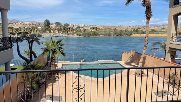 A pool area with a view of a lake, surrounded by palm trees and a mountainous landscape. - Luxury Riverfront Home w/ Pool • Private Boat Dock • Minutes to Laughlin (Bullhead City)