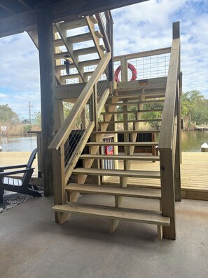 A wooden staircase leading to a covered area with a view of a body of water and a dock. - Seafood and fishing time. Book your fishing trip catch specks and reds. (Chauvin)