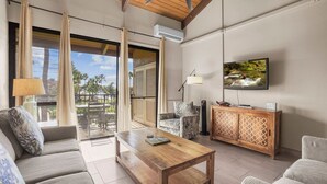 A modern living room with a wooden coffee table, two sofas, a patterned armchair, a cabinet, and a television on the wall. - Summer DEALS-A/C-Pool-Oceanview Building 1 ! (Kihei)
