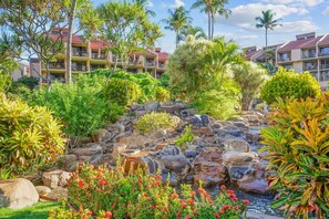A resort with a landscaped garden featuring a rock waterfall, palm trees, and tropical plants.