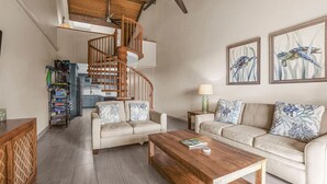 A spacious living area with a wooden staircase, two sofas with patterned cushions, a coffee table, and artwork on the walls. - Summer DEALS-A/C-Pool-Oceanview Building 1 ! (Kihei)