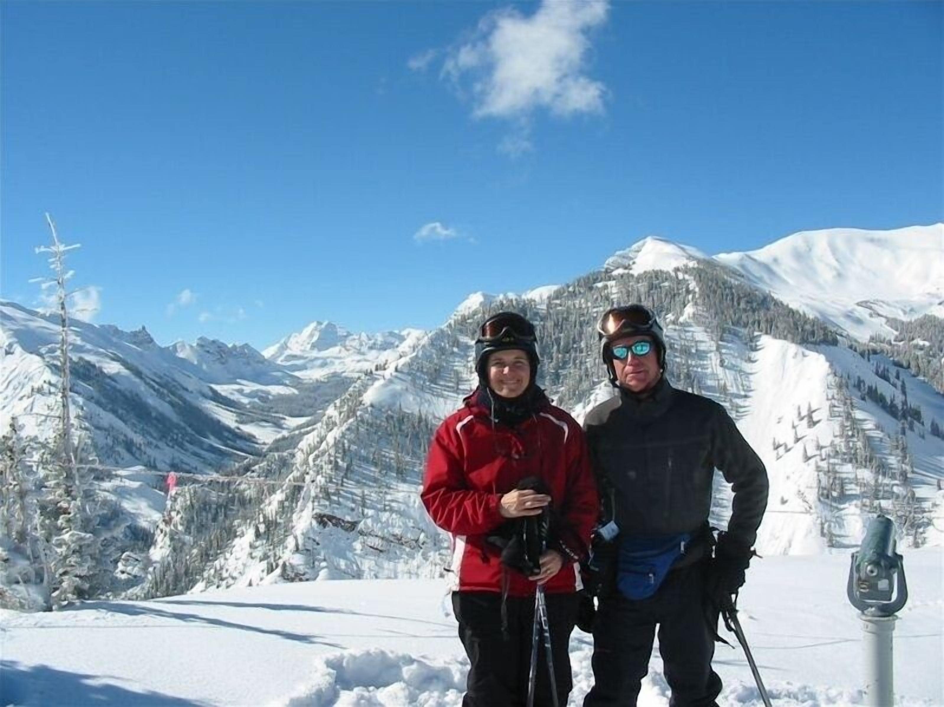 Two people standing in a snowy mountainous area with a clear sky.
